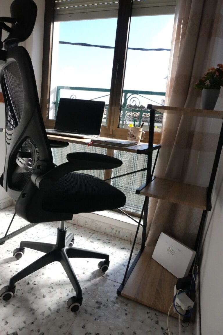 Escritorio con laptop y silla ergonómica junto a una ventana
